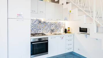Une cuisine moderne avec des meubles blancs, un crédence à motifs, une cuisinière à gaz, un four et un four à micro-ondes.