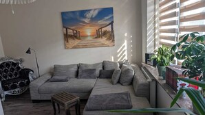 Een woonkamer met een grote bank, een kleine houten tafel en een schilderij van een zonsondergang aan de muur.