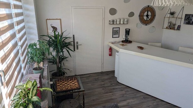 Een knus woongedeelte met een kitchenette, een deur, een klein tafeltje met een schaakbord en verschillende potplanten.