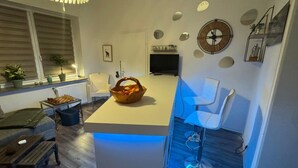 Een moderne keuken met een centraal eiland, barstoelen, een televisie en decoratieve wandelementen.