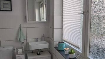 Uma casa de banho moderna com sanita, lavatório e espelho. Tem uma janela com estores e vista para o exterior.