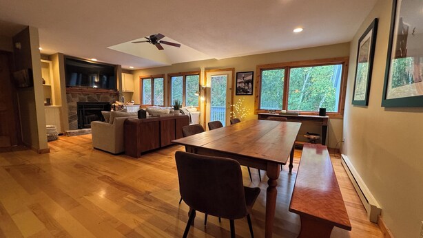 A spacious kitchen with a dining area, wooden flooring, and large windows offering a view of the outdoors.