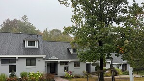 A two-story building with a grey exterior, a small porch, and a well-maintained garden with various plants and flowers.