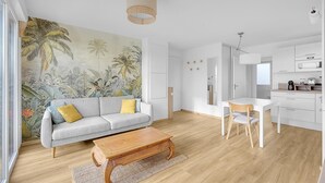 Een moderne woonkamer met een grijze bank, een houten salontafel en een tropische muurschildering.