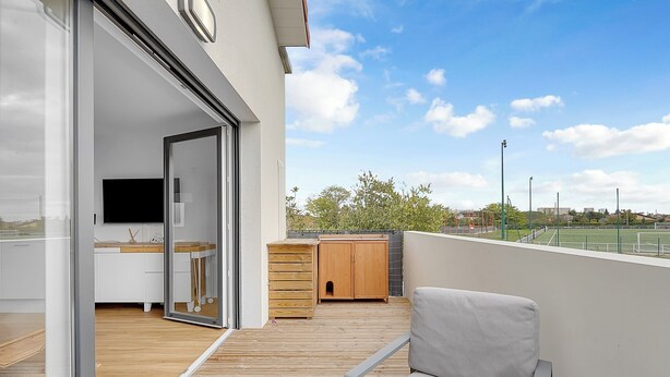 Een balkon met een houten terras, een bank, een houten kast en een televisie.