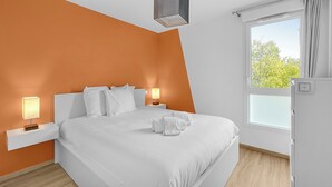 Een moderne hotelkamer met een groot bed, wit beddengoed, twee nachtlampen, een raam met gordijnen en een unieke geometrische lamp.