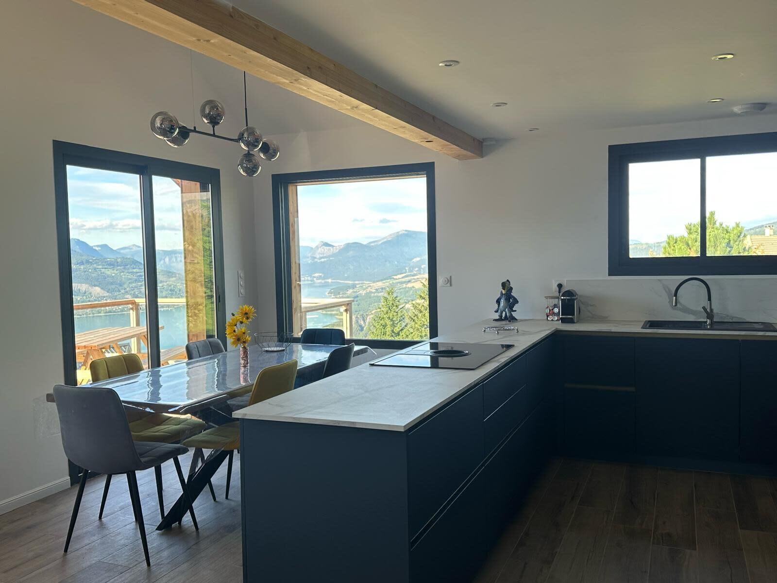 Une cuisine moderne dotée de grandes fenêtres, d’un coin repas et offrant une vue sur un lac et des montagnes.