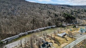 Ländliche Landschaft mit Fluss, Brücke und einer kleinen Ansammlung von Gebäuden, darunter ein Haus und ein Stall.