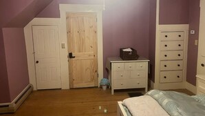 Ein Schlafzimmer mit Holztür, weißem Schminktisch, Nachttisch und Bett.