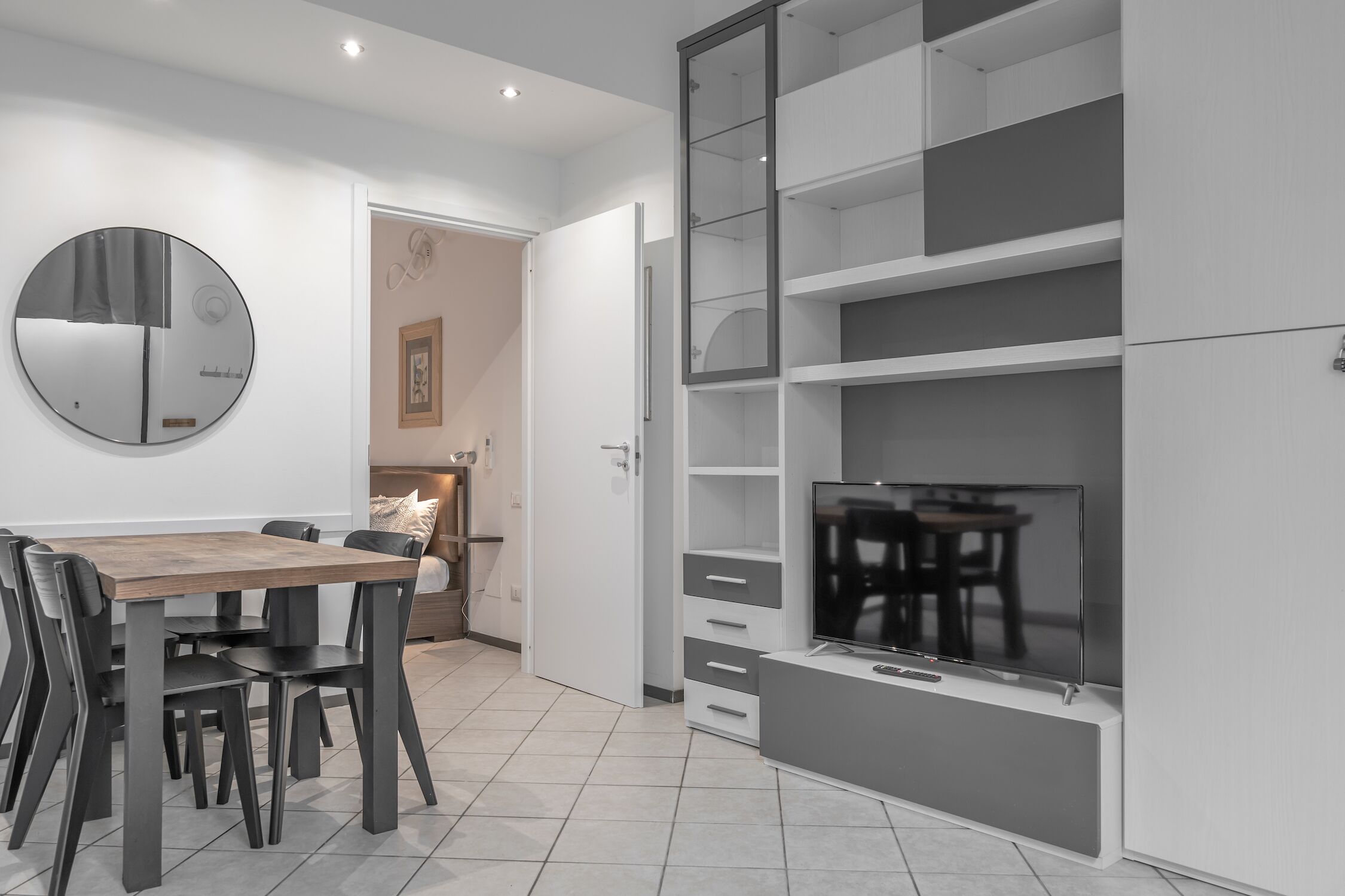 A modern kitchen with a dining table, chairs, a TV, and built-in shelving.