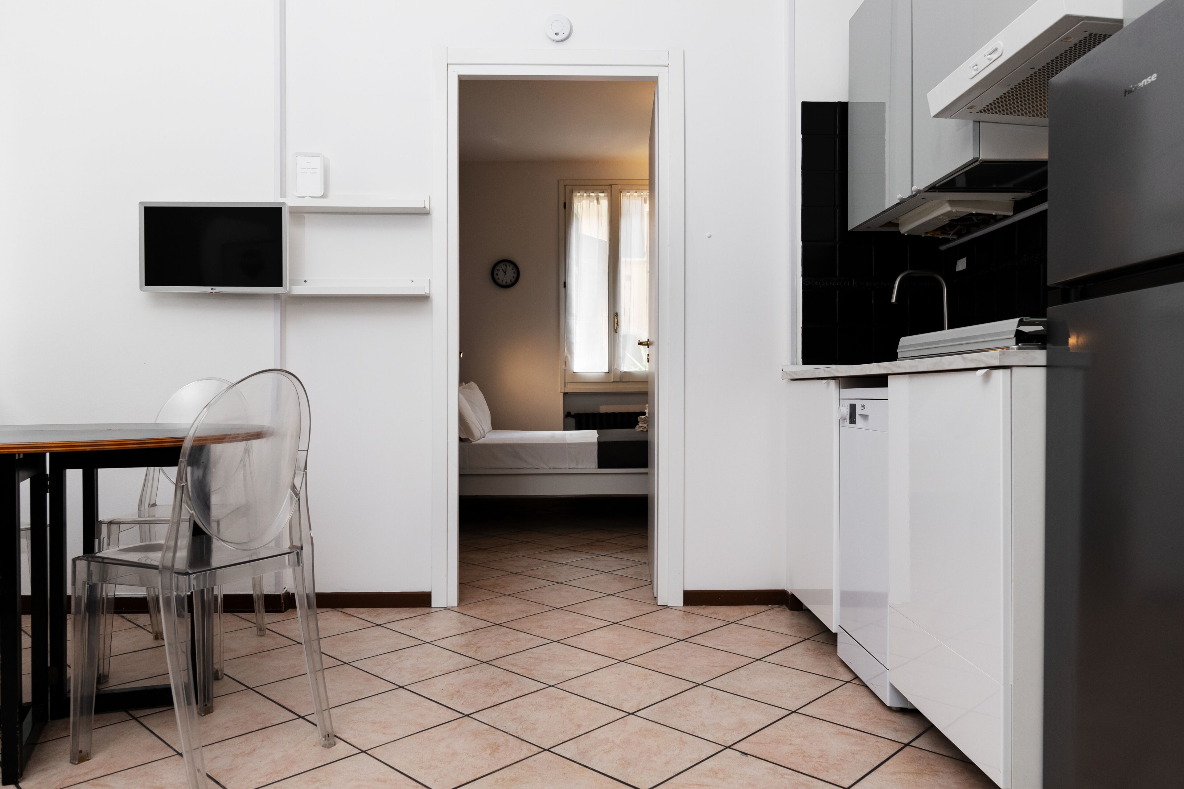 Cocina compacta con comedor, televisor integrado y dormitorio visible con cama y cortinas.