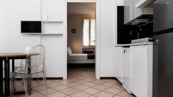 Cocina compacta con comedor, televisor integrado y dormitorio visible con cama y cortinas.