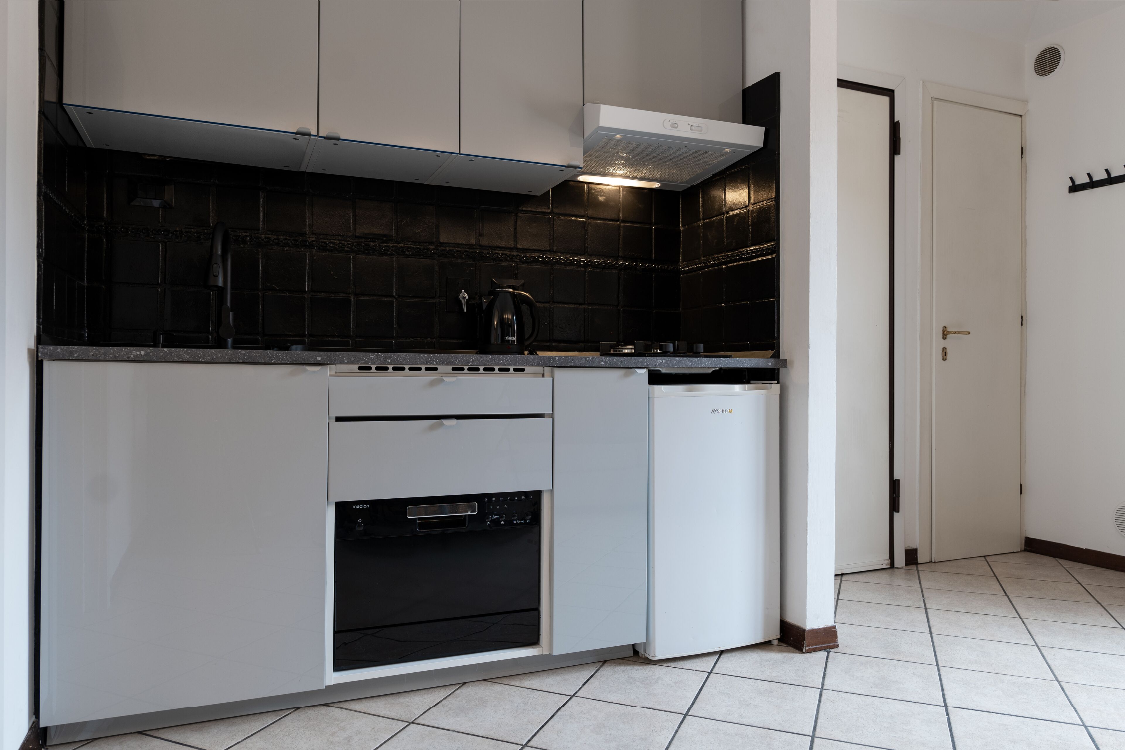 A kitchen with white cabinets, a black tiled backsplash, a built-in oven, and a dishwasher.