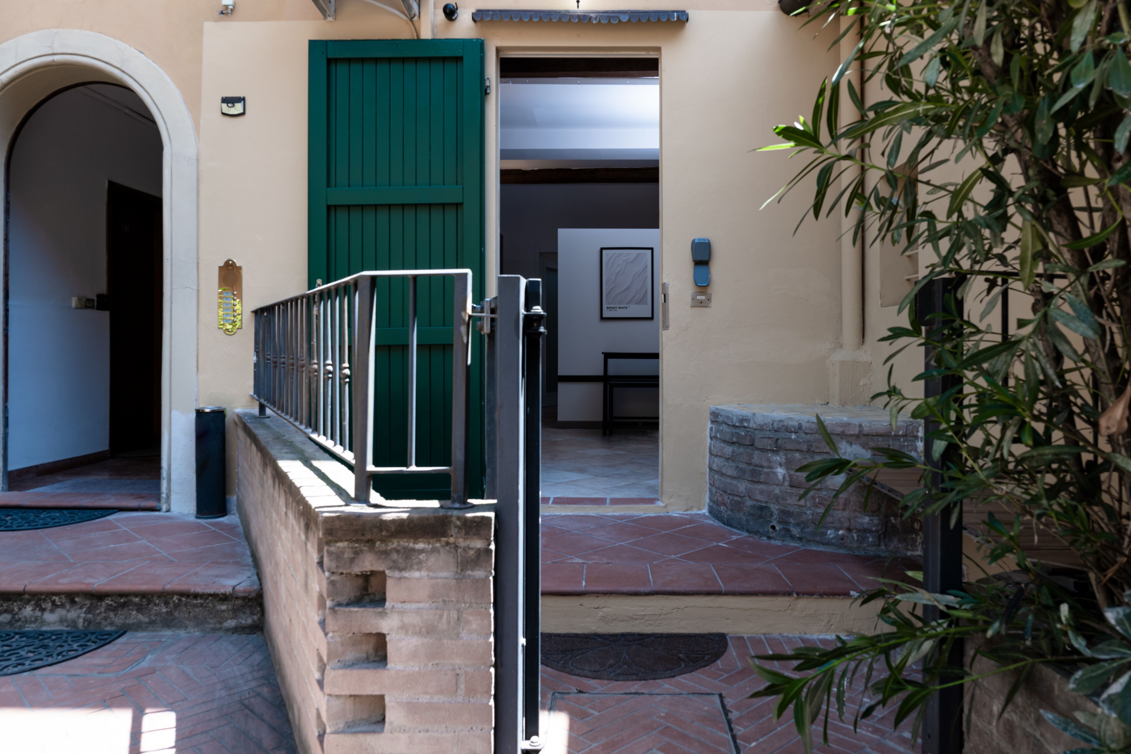 Entrada de un edificio con puerta verde, un portón de metal y un banco de piedra.
