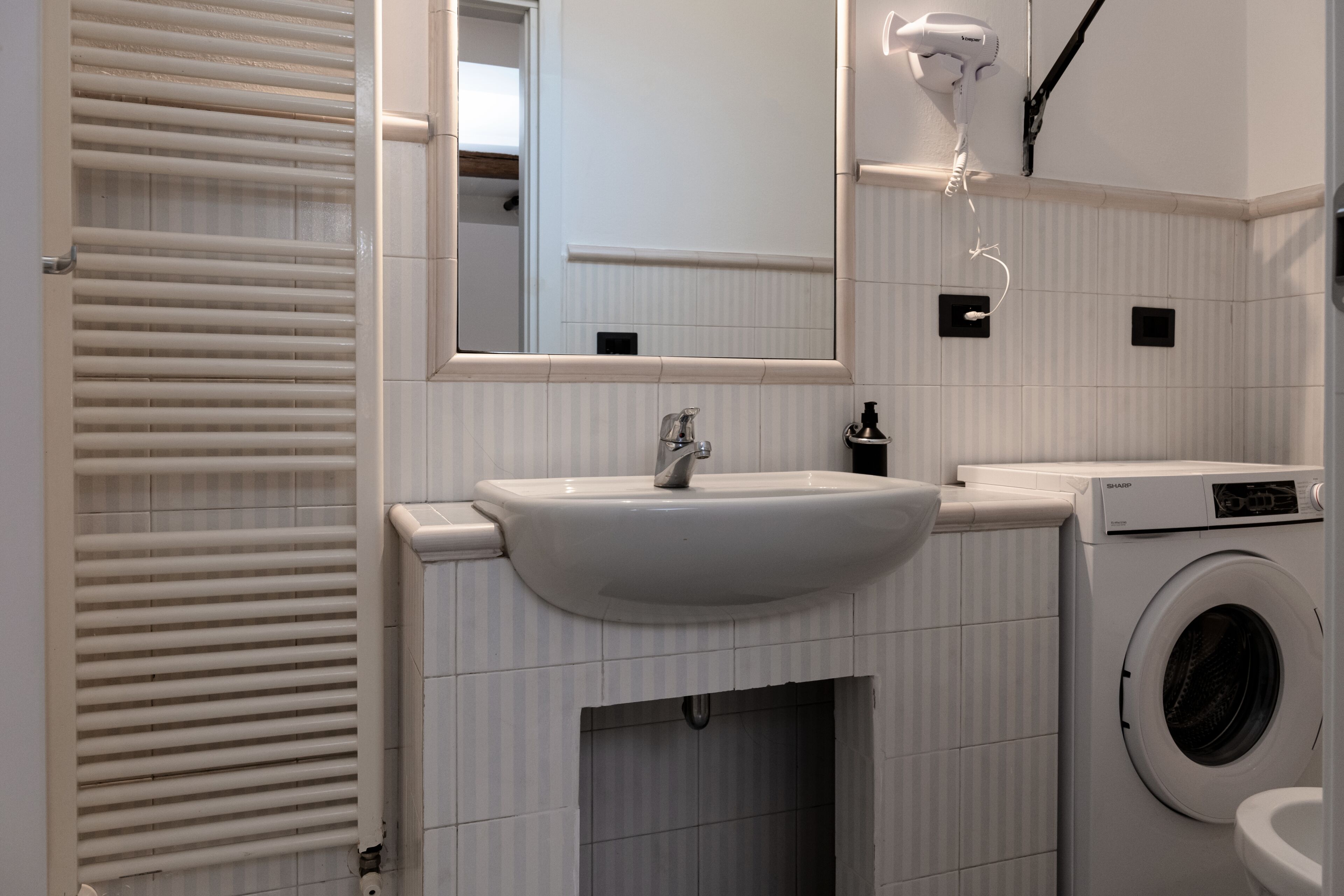A bathroom with a sink, mirror, towel rack, and a washing machine.