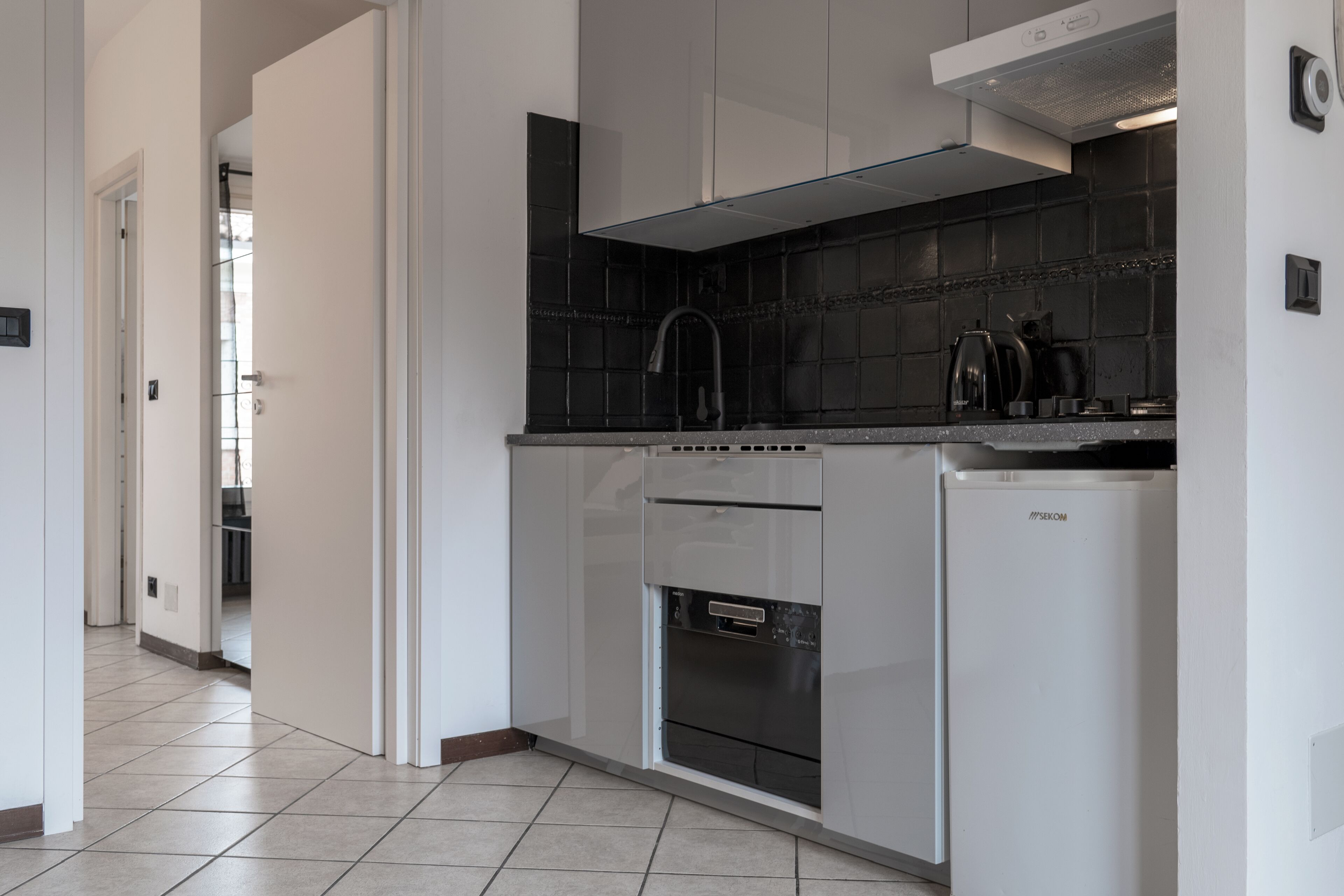 Een moderne keuken met witte kasten, een zwart betegelde spatwand en een inbouwoven.