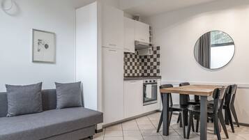 Eine moderne Küche mit weißen Schränken, einer karierten Spritzschutzwand, einem runden Spiegel und einem Essbereich mit einem Holztisch und schwarzen Stühlen.
