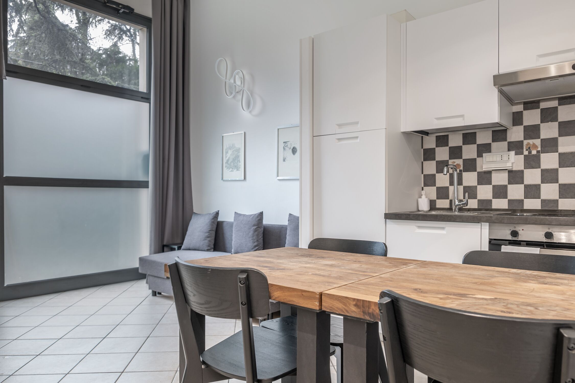 A modern kitchen with a checkered backsplash, a wooden dining table, and a gray sofa.