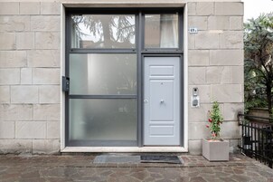 Ingresso di un edificio moderno con un'ampia porta in vetro, una piccola pianta in vaso e una cassetta delle lettere a parete.