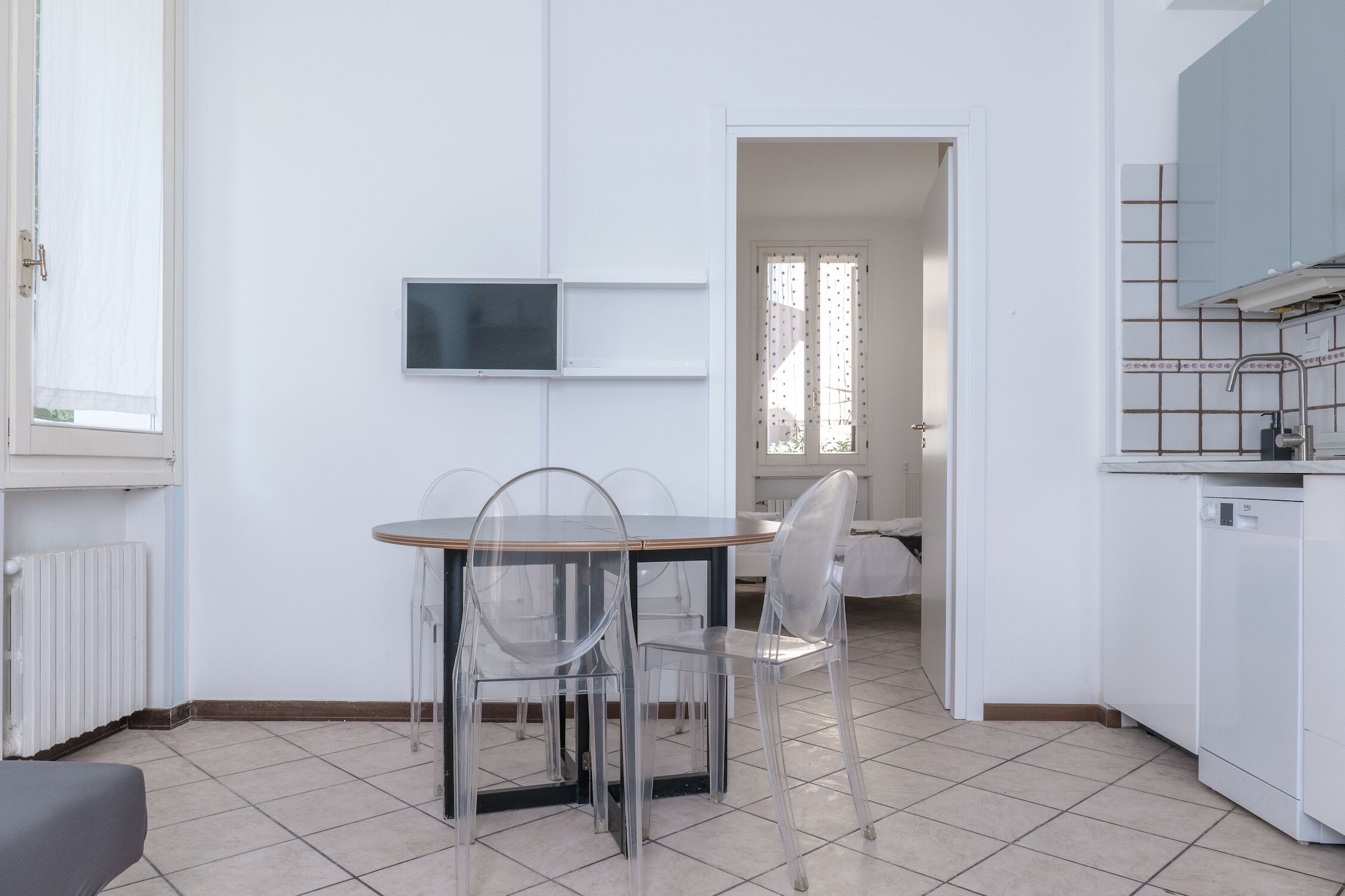 A modern kitchen with white cabinets, a built-in dishwasher, and a dining area with a round table and clear chairs.