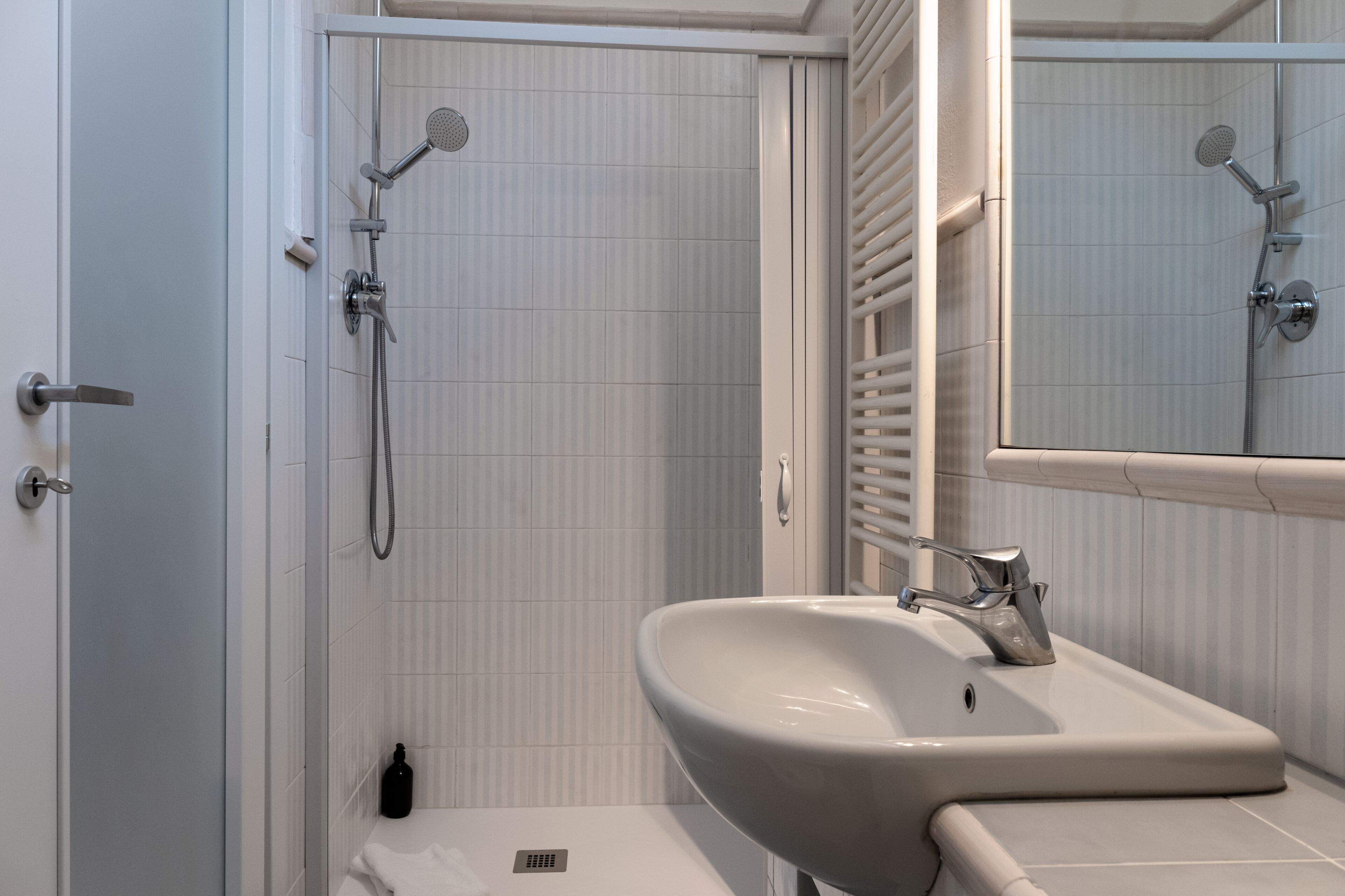 Een badkamer met een wit wastafelmeubel, een spiegel, een douche met een handdouche en een handdoekrek.