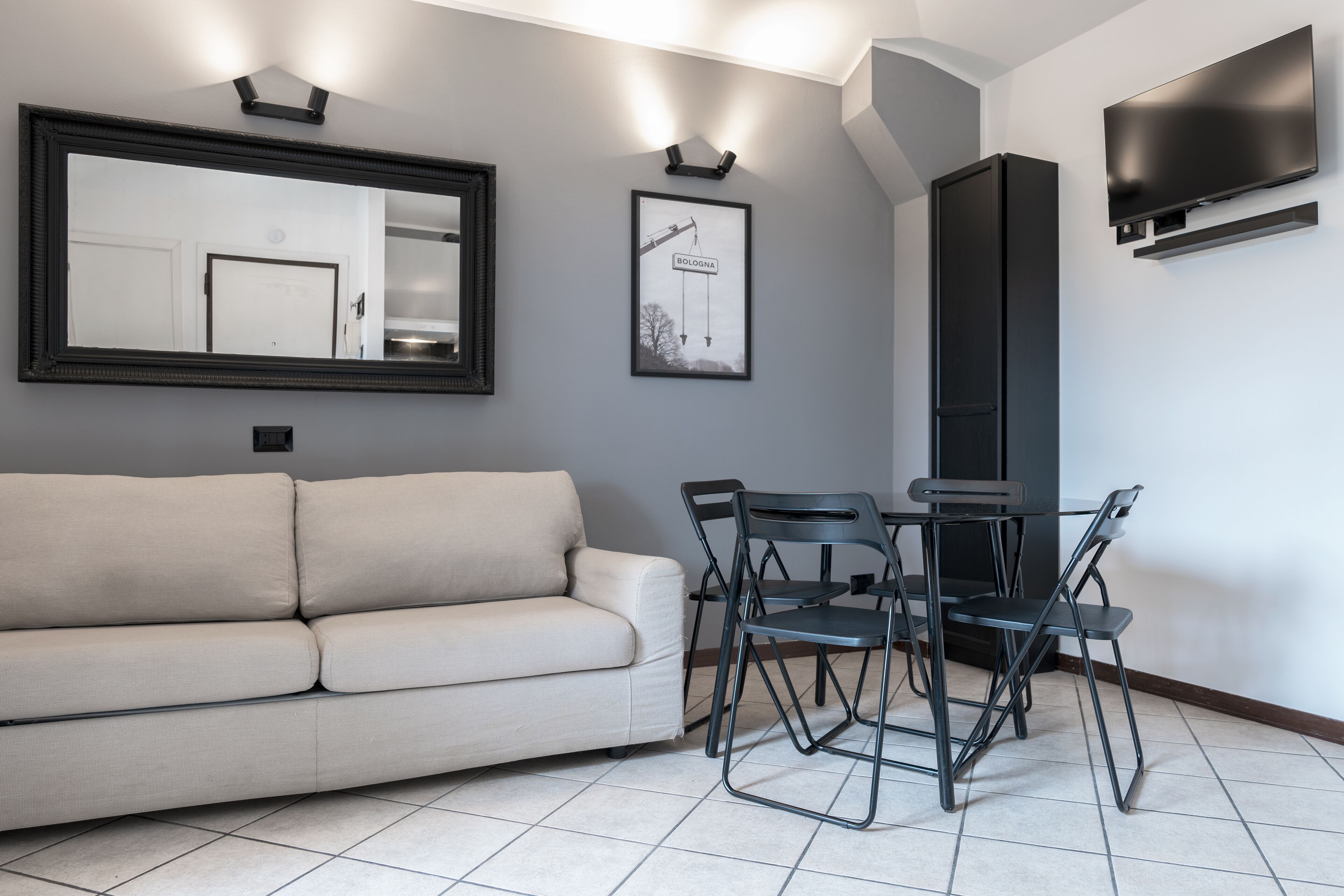 Una sala moderna con un sofá, una mesa de comedor con sillas, un espejo grande, un cuadro enmarcado, un televisor de pantalla plana y un mueble alto.