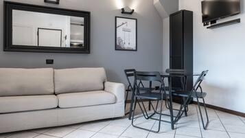 Una sala moderna con un sofá, una mesa de comedor con sillas, un espejo grande, un cuadro enmarcado, un televisor de pantalla plana y un mueble alto.