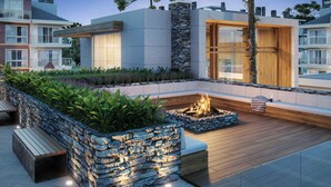 A modern outdoor patio with a stone fire pit, wooden benches, and lush greenery. - Veneto Residential / 2 Suites / 8 PAX / By HOUSINGCEARA (Gramado)