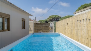 Une piscine dont le fond est carrelé, entourée d’une clôture en bois et bordée d’un bâtiment doté de fenêtres.