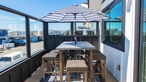 A balcony with a table and chairs, a striped umbrella, and a view of the city. - Walk to beach, 3/2 w/Views, Deck & Accessibility (Cayucos)