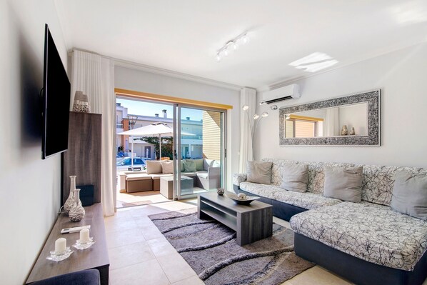 A modern living room with a sofa, a coffee table, a flat-screen TV, and a large mirror.