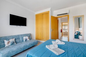 A hotel room with a sofa, a bed, a TV, a wardrobe, and a mirror.