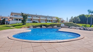 Une piscine à bord incurvé, entourée de chaises longues et avec un bâtiment en arrière-plan.