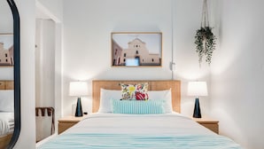 A hotel room with a bed, two bedside tables, a hanging plant, a framed picture on the wall, and a window with a view of buildings. - Condado Flat Swimming Spot Garden Haven (San Juan)