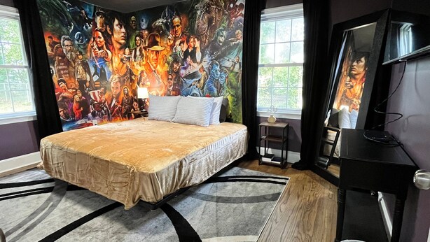 A bedroom with a large bed, a wall mural, a TV, and a window. - Movie Magic: The Scene-Stealer (Winston-Salem)