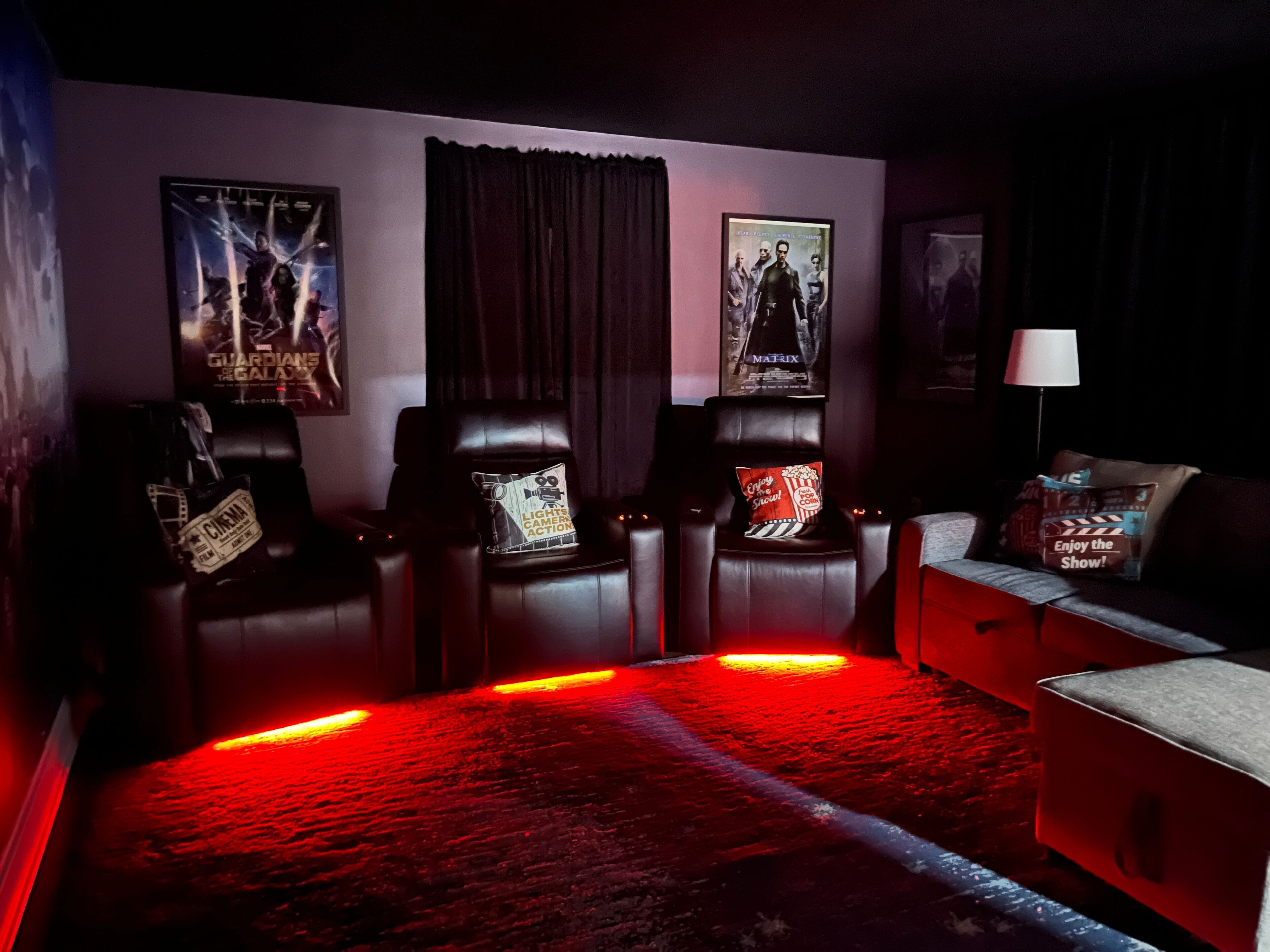 Une salle de cinéma à l’ambiance sombre, dotée de fauteuils inclinables en cuir, d’un éclairage d’ambiance rouge et d’affiches de films aux murs.