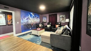 A living room with a large wall mural, a grey sofa, a coffee table, and a red accent piece. - Movie Magic: The Scene-Stealer (Winston-Salem)