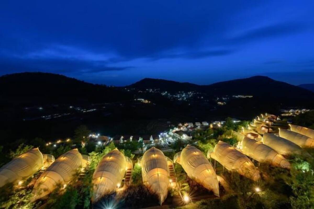 A series of elongated, tent-like structures with lights, set against a mountainous backdrop at night.