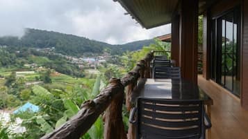 A balcony with a view of a valley and mountains, wooden railings, and a table with chairs.