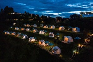 A series of dome-shaped tents arranged in rows on a grassy slope, with a staircase leading up to a building in the background. - Mon View Ngam (Mae Rim)
