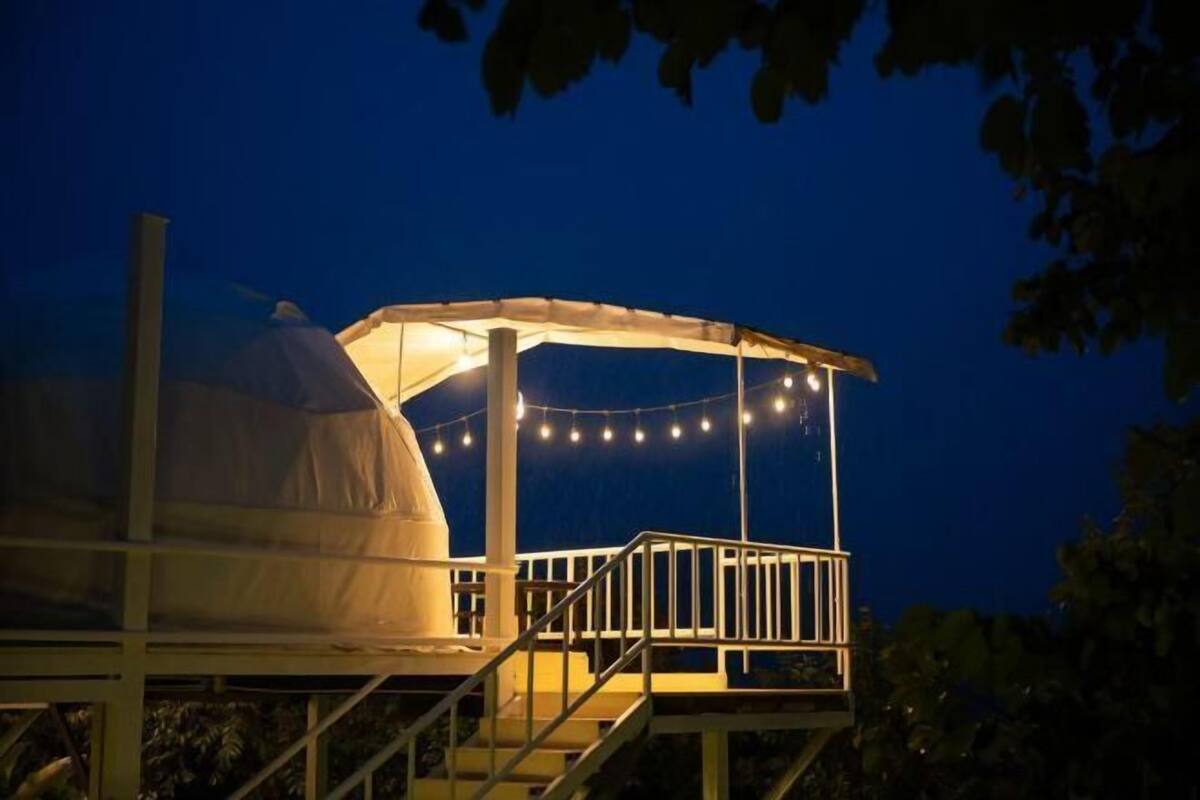 A gazebo with a covered seating area and string lights, surrounded by a wooden deck and stairs.