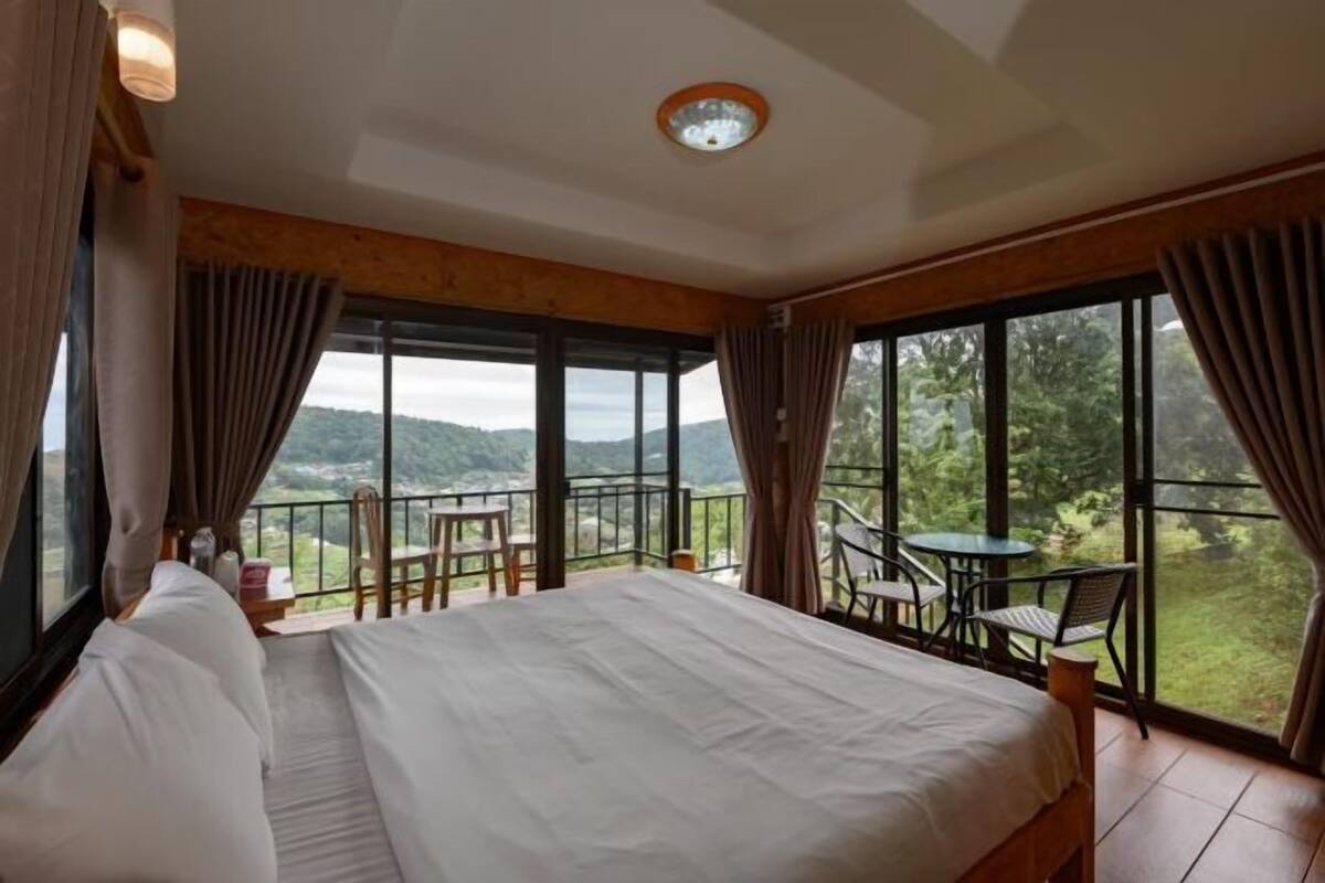 A bedroom with a large bed, a balcony with chairs, and a view of the outdoors.