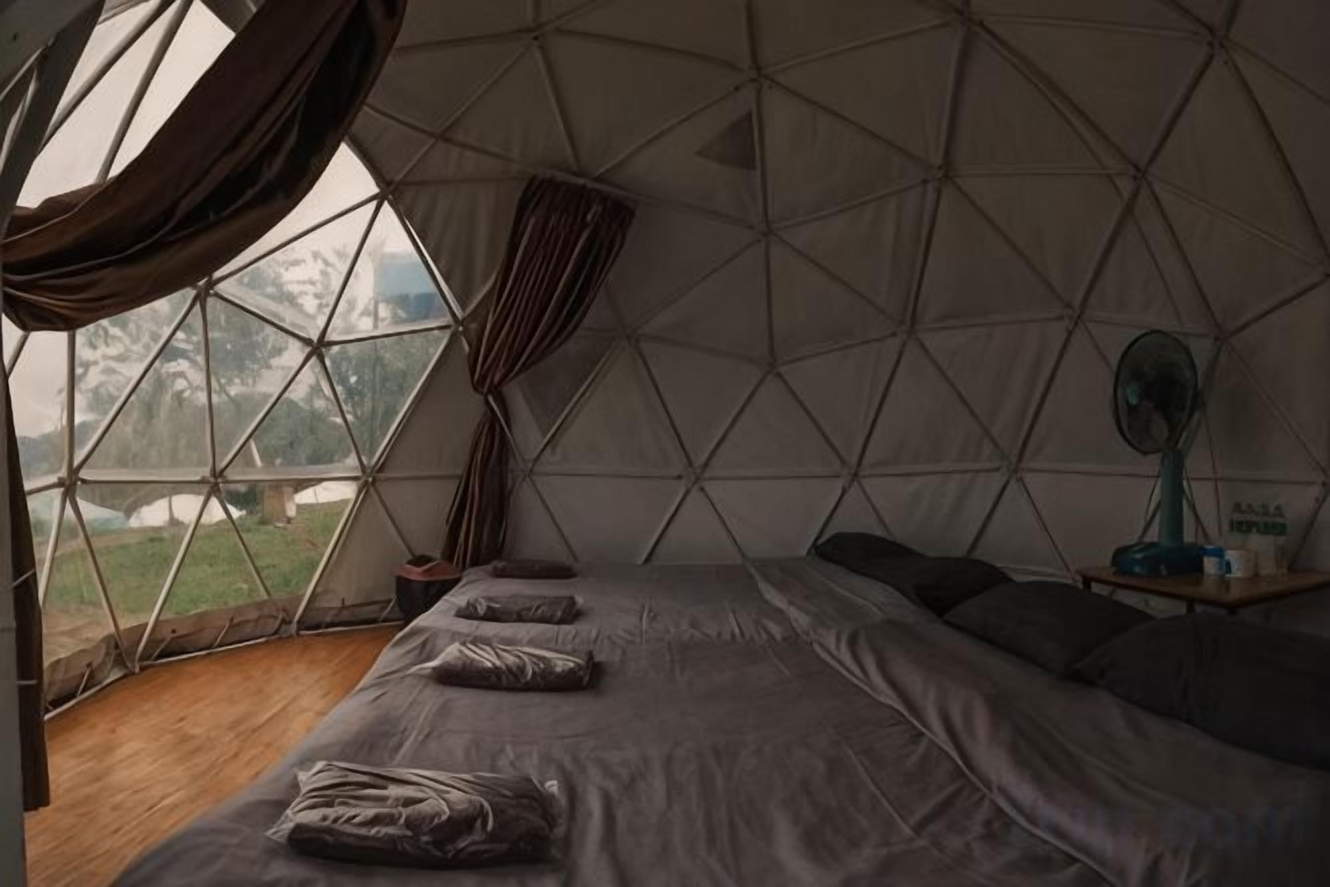 Una tienda de campaña con cama, un ventilador y vistas al exterior.