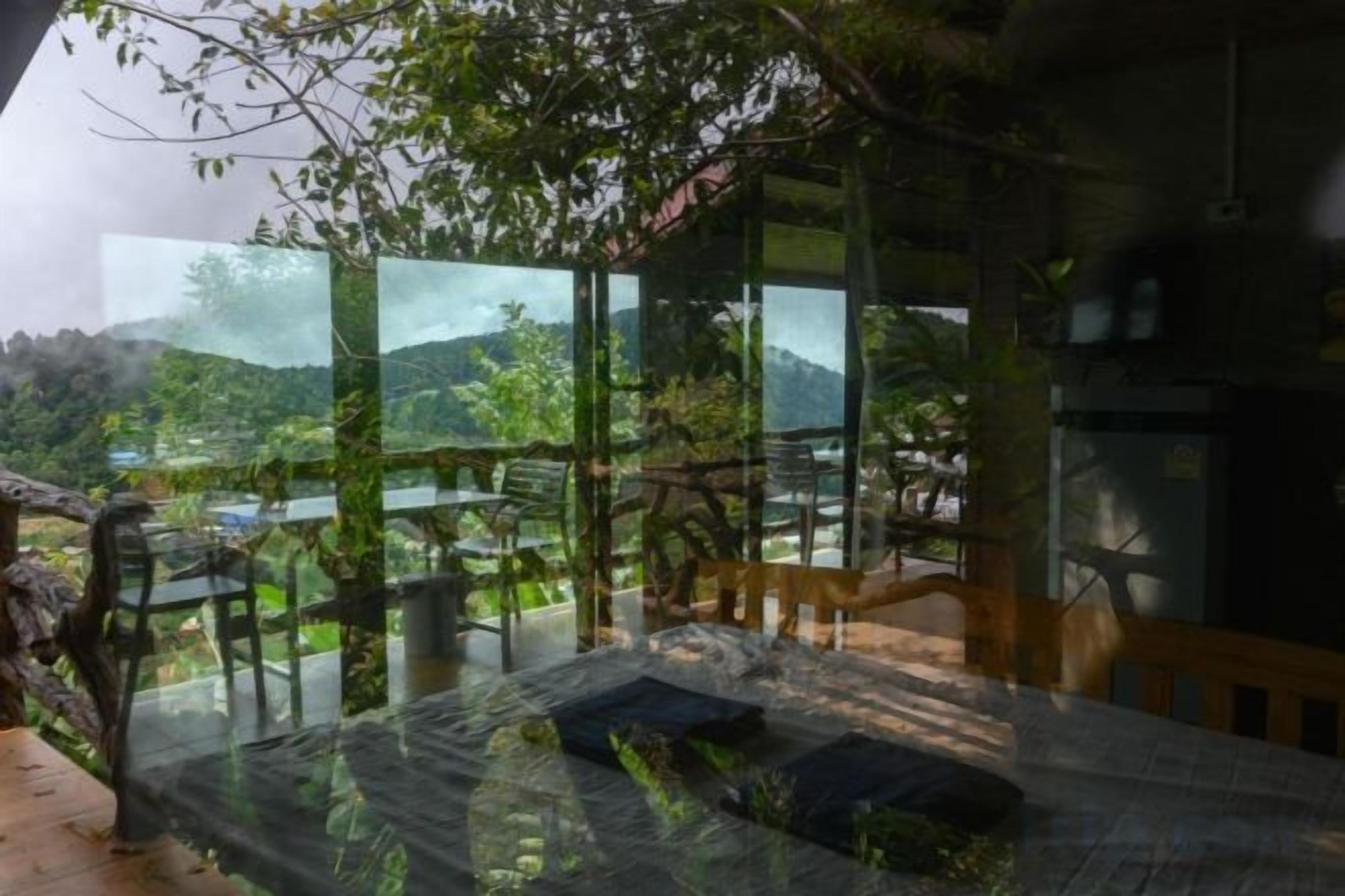 Una habitación con pared de vidrio, una cama y vista a un paisaje montañoso.