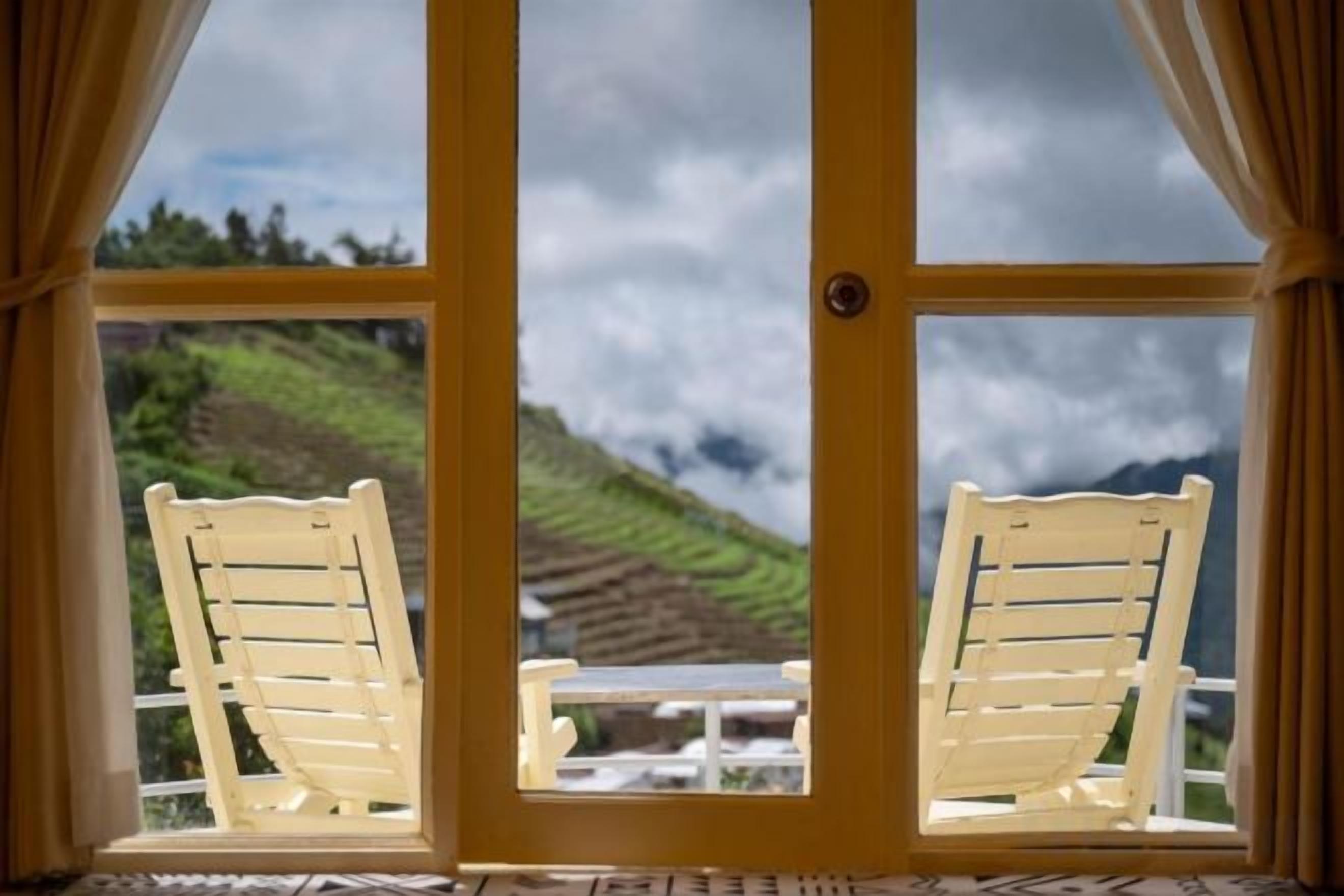 Una habitación con dos sillas de madera frente a un ventanal.