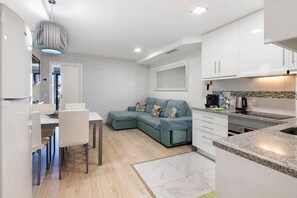 Une cuisine moderne avec des meubles blancs, un coin repas comprenant une table et des chaises, et un canapé d’angle gris.