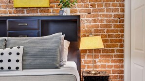 A bed with a headboard, pillows, a bedside lamp, and a small table with books. - Savannah Serendipity | Historic Broughton St (Savannah)