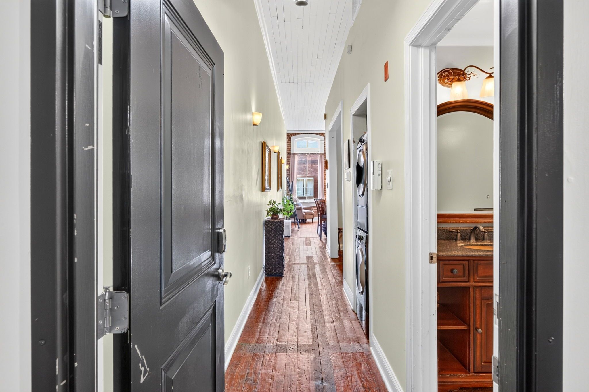 A hallway with a wooden floor, a dining area with chairs and a table, and a kitchen area with cabinets and a sink.