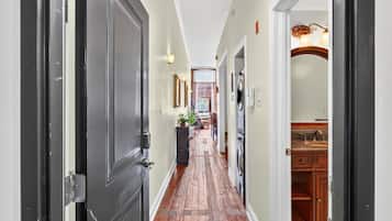 A hallway with a wooden floor, a dining area with chairs and a table, and a kitchen area with cabinets and a sink.