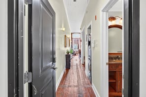 A hallway with a wooden floor, a dining area with chairs and a table, and a kitchen area with cabinets and a sink.